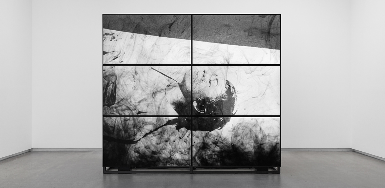 A bank of six screens displays a film featuring archival images with plumes of ink.
